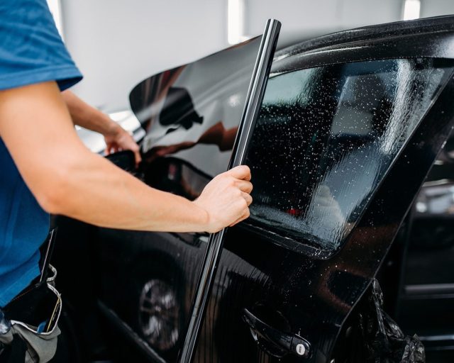 Technician installing window tint film on a car's rear side window